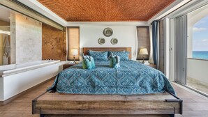 Een slaapkamer met een groot bed, een houten hoofdeinde, uitzicht op zee en een bakstenen plafond.