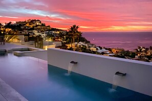 Una piscina en la azotea con fuentes y vistas a un pueblo costero al atardecer.