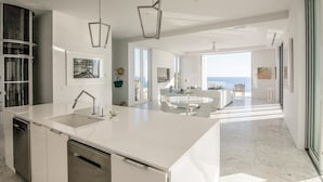 Een moderne keuken met een groot eiland, roestvrijstalen apparatuur en uitzicht op de woonkamer.