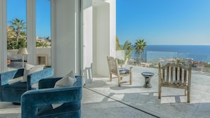 Een moderne woonkamer met uitzicht op de oceaan, met een blauwe bank, een houten stoel en een kleine tafel.