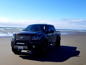 Una camioneta pickup negra estacionada en una playa arenosa con el océano al fondo.