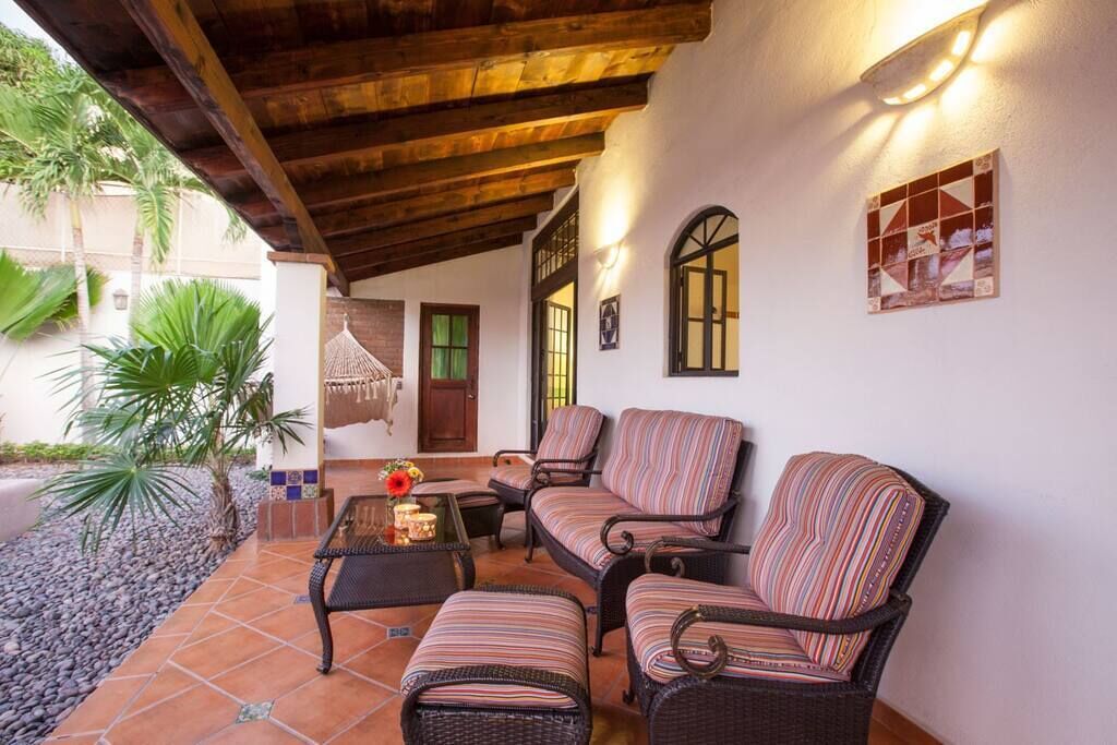 A covered patio area with wicker furniture, a small table with a vase, and a wall-mounted light fixture.