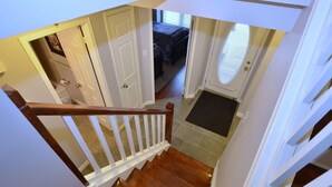 Una escalera conduce a un dormitorio con una puerta, un felpudo y una ventana con persianas.