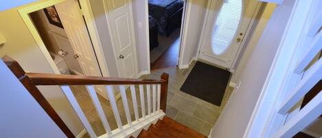 Una escalera conduce a un dormitorio con una puerta, un felpudo y una ventana con persianas.