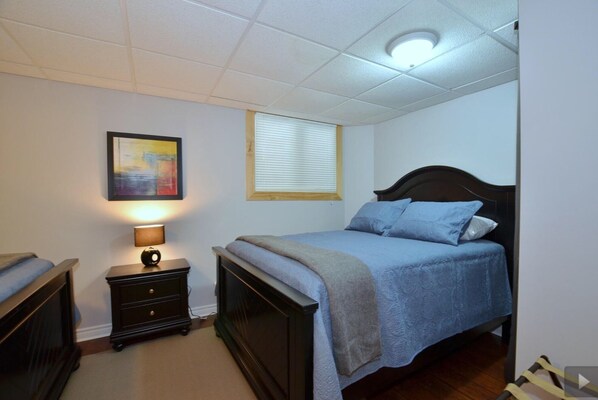 Un dormitorio con cama, una mesita de noche, una lámpara, una ventana con persianas y una luz en el techo.