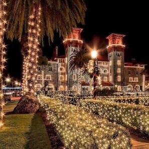 Un edificio parecido a un castillo con múltiples torres, rodeado de un jardín bien iluminado con luces en forma de estrella.
