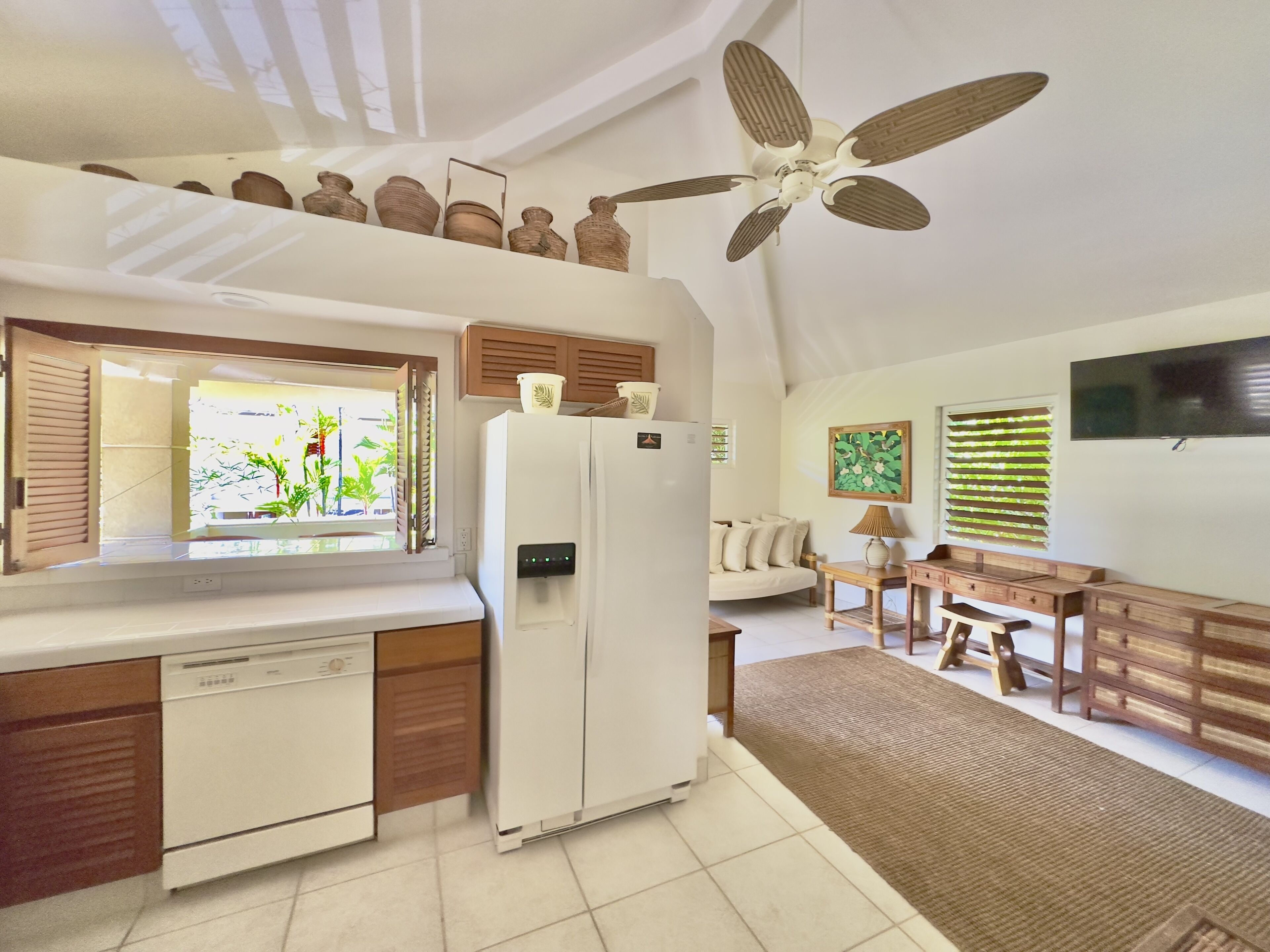A compact kitchen with a built-in dishwasher, a refrigerator, and a window with a view of greenery.