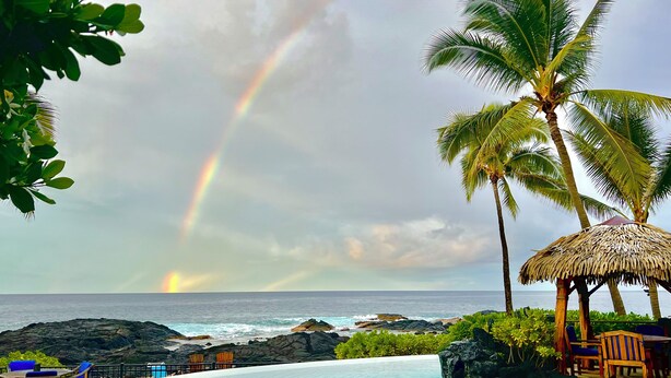 A poolside area with a view of the ocean, a thatched-roof structure, and a rainbow. - Exotic Kona Bay Hawaii Beachfront Tropical Paradise Stunning Home. (Kailua-Kona)