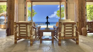 A room with a view of the ocean, featuring two wooden chairs, a small table, and a statue. - Exotic Kona Bay Hawaii Beachfront Tropical Paradise Stunning Home. (Kailua-Kona)