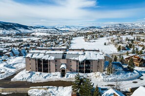 Un hôtel à plusieurs étages, dont le toit est recouvert de neige, situé dans une région montagneuse et offrant une vue sur les bâtiments environnants et le paysage enneigé.