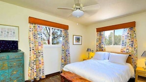A bedroom with a bed, wooden bench, dresser, and curtains. - Peaceful Hilltop Casita w/ Stunning Views, Close to the Historic Plaza (Santa Fe)