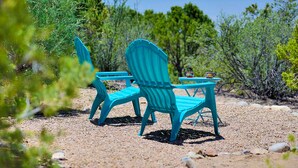 A turquoise outdoor seating area with two chairs and a small table, surrounded by natural vegetation and rocks. - Peaceful Hilltop Casita w/ Stunning Views, Close to the Historic Plaza (Santa Fe)