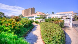A pathway leading to a building with a white facade and a red roof, surrounded by lush greenery and a tall hotel in the background. - 🌞Updated Condo-Private Path to Beach~3BR St Martin Beachwalk Villas 131 (Destin)