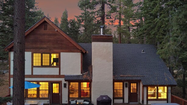 Una casa de madera de dos pisos con un balcón, ventanas grandes y una chimenea.