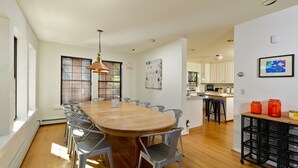 Una cocina moderna con armarios blancos, una isla de madera y un comedor con una mesa larga y sillas metálicas.