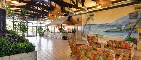 A spacious lobby with a high ceiling, wooden beams, a mural of a tropical beach, and comfortable seating areas.