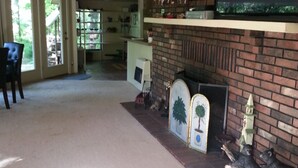 Ein Wohnzimmer mit Kamin, einem darüber angebrachten Fernseher und einem Essbereich mit Tisch und Stühlen.