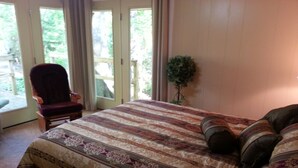Ein Schlafzimmer mit einem großen Bett, einem Sessel und Blick ins Freie durch eine Glastür.
