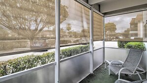 A balcony with two chairs, large windows, and a view of a street and trees. - Short/Long Stays; Sun, Fun, & Relax in the Gardens.  (Palm Beach garden)