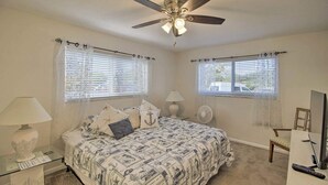 A bedroom with a bed, two bedside tables, a ceiling fan, a chair, a desk with a computer, and two windows with blinds. - Short/Long Stays; Sun, Fun, & Relax in the Gardens.  (Palm Beach garden)