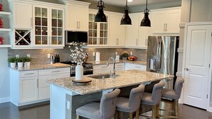 Une cuisine moderne avec des meubles blancs, un îlot central doté de tabourets et des luminaires suspendus.