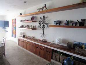 Un salon avec des étagères en bois où sont exposés des objets décoratifs, un téléviseur fixé au mur et un sol carrelé.