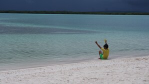Una persona sentada en una playa arenosa junto a un mar tranquilo bajo un cielo nublado.