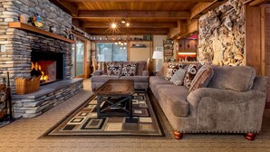 A cozy living room with a stone fireplace, wooden ceiling beams, and a large sofa. - Oceanfront Vacation Home - Spectacular Views; Hot Tub; Wi-Fi. (Elk)