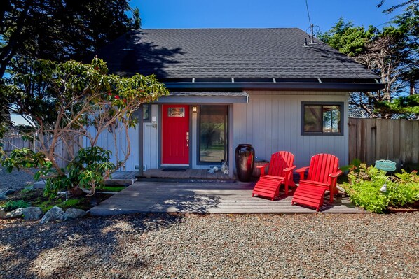 Ein Haus mit roter Tür, einer kleinen Veranda mit roten Stühlen und einem Schotterweg.