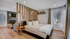 A modern bedroom with a large bed, a wooden headboard, a TV mounted above a fireplace, and a window with curtains. - Canyons Hidden Creek Studio on the Duck  Pond (Park City)