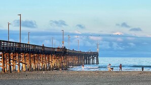 Une jetée qui s’avance dans la mer, avec des personnes qui la traversent, et la plage au premier plan.