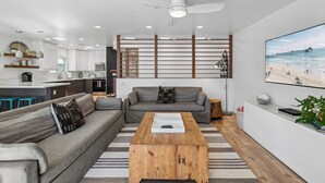 Un salon moderne avec un canapé gris, une table basse en bois et un grand tableau sur le thème de la plage accroché au mur.