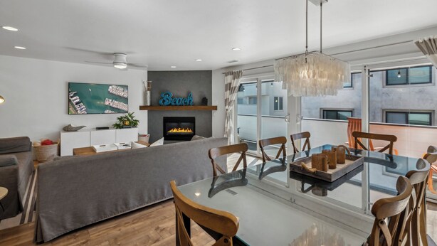 Un salon moderne avec une cheminée, un coin repas doté d’une table en verre et une grande fenêtre offrant une vue sur la ville.