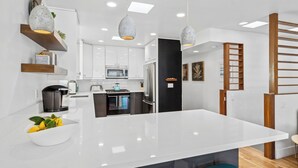 Une cuisine moderne avec des meubles blancs, un îlot central et des luminaires suspendus.