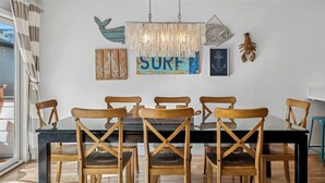 Un espace repas avec une table et des chaises en bois, un lustre et des œuvres d’art murales, notamment un panneau indiquant « SURF » et des illustrations de poulpes.
