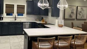 A modern kitchen with dark cabinets, a large island, and pendant lighting. - Seacrest Luxury Beach House - Sleeps 14 (Seacrest Beach)