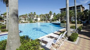 A swimming pool with lounge chairs, palm trees, and hotel buildings in the background. - Seacrest Luxury Beach House - Sleeps 14 (Seacrest Beach)