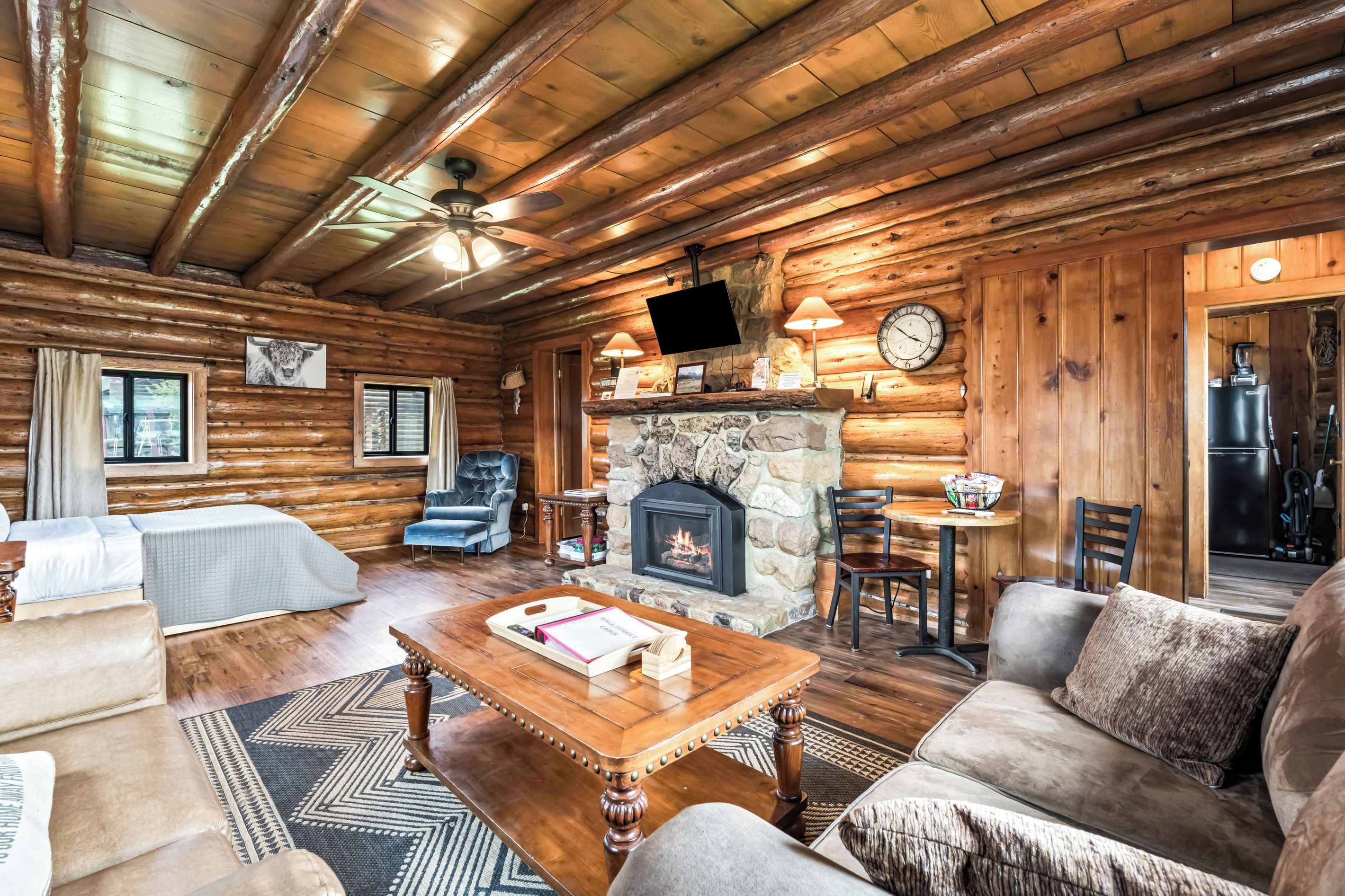L’intérieur d’une cabane en rondins comprend une cheminée, un coin salon et un téléviseur fixé au mur.
