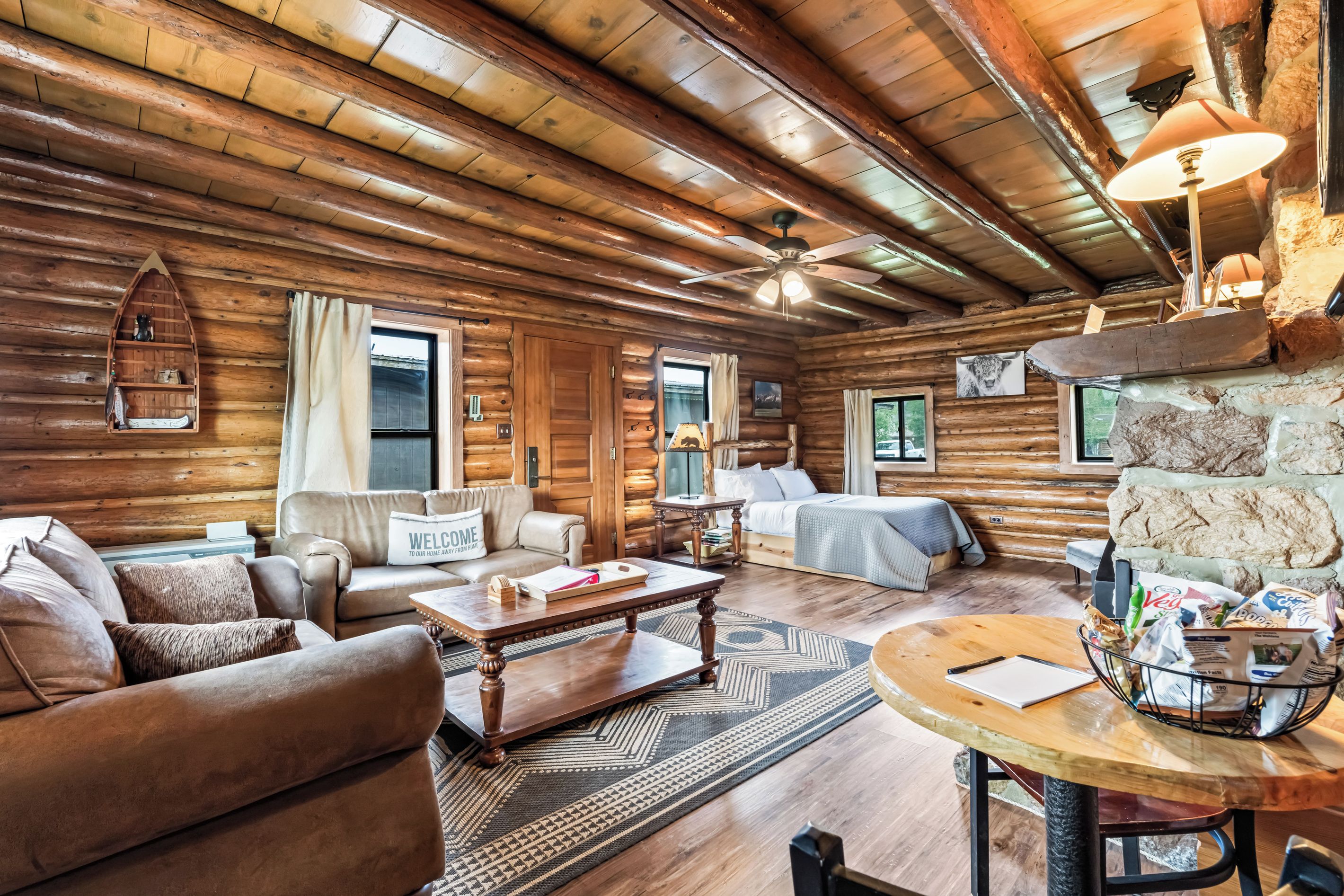 A log cabin interior with a living room, a sofa, a coffee table, and a dining area.