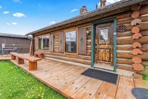 A log cabin with a deck, a bench, and a door with a number.