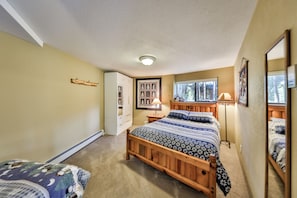 A bedroom with a wooden bed, a nightstand, a lamp, a window with a view of trees, and a wall-mounted coat rack. - COZY, sunny, 5 big bedrooms, 3 baths, 3500 sq ft, Trees, 4 miles to Winter Park (Fraser)