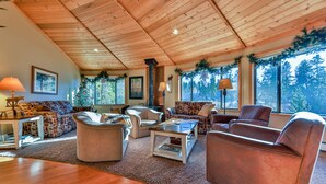 Un salon chaleureux avec des poutres apparentes en bois au plafond, de grandes fenêtres décorées pour Noël et différents types de sièges.