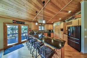 A modern kitchen with wooden cabinets, a stainless steel refrigerator, and a bar area with stools.