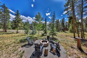 An outdoor seating area with Adirondack chairs and a fire pit, surrounded by a forested landscape.