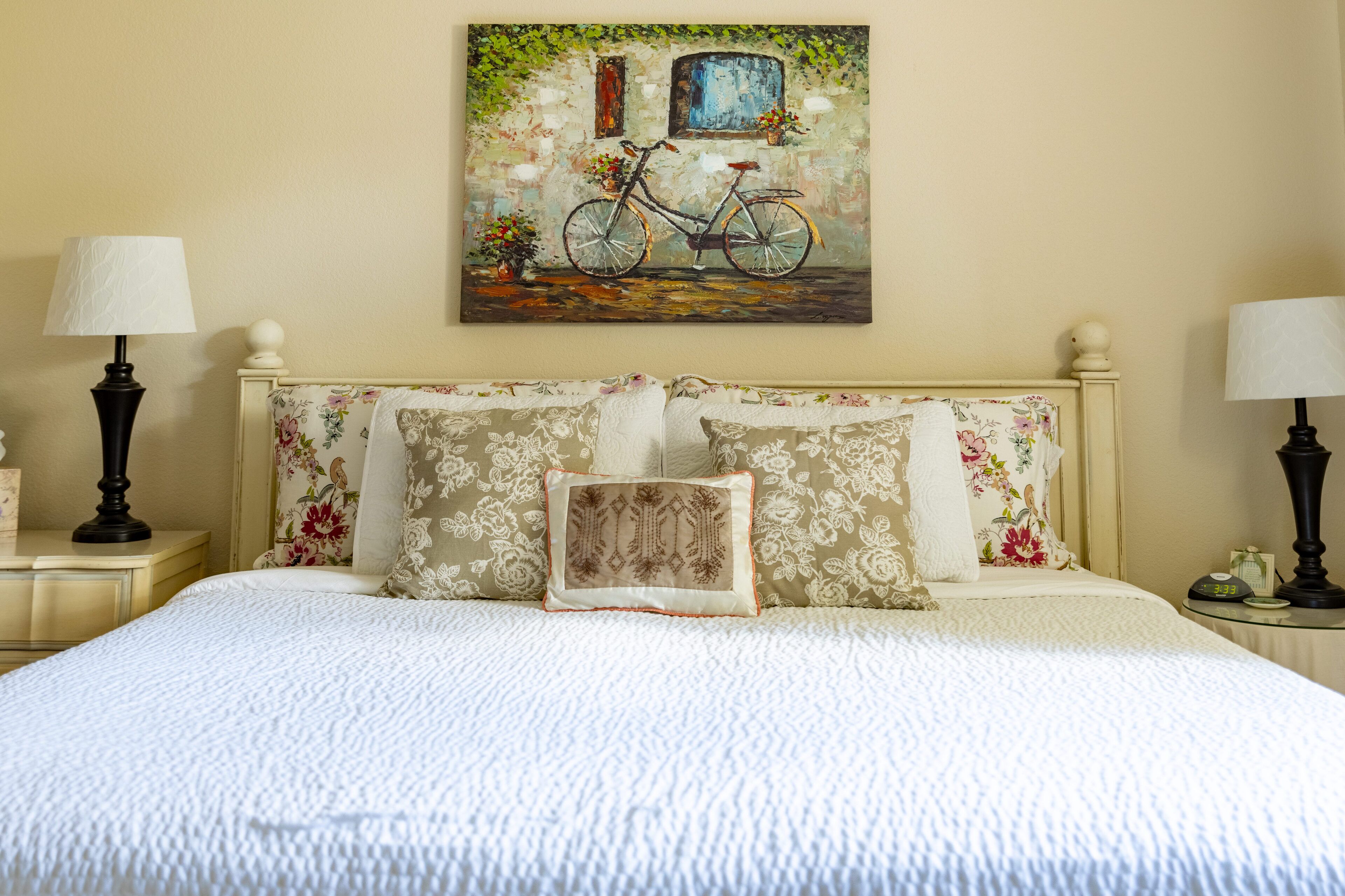 Una cama bien hecha con almohadillas estampadas con motivos florales y un cuadro de una bicicleta en la pared.