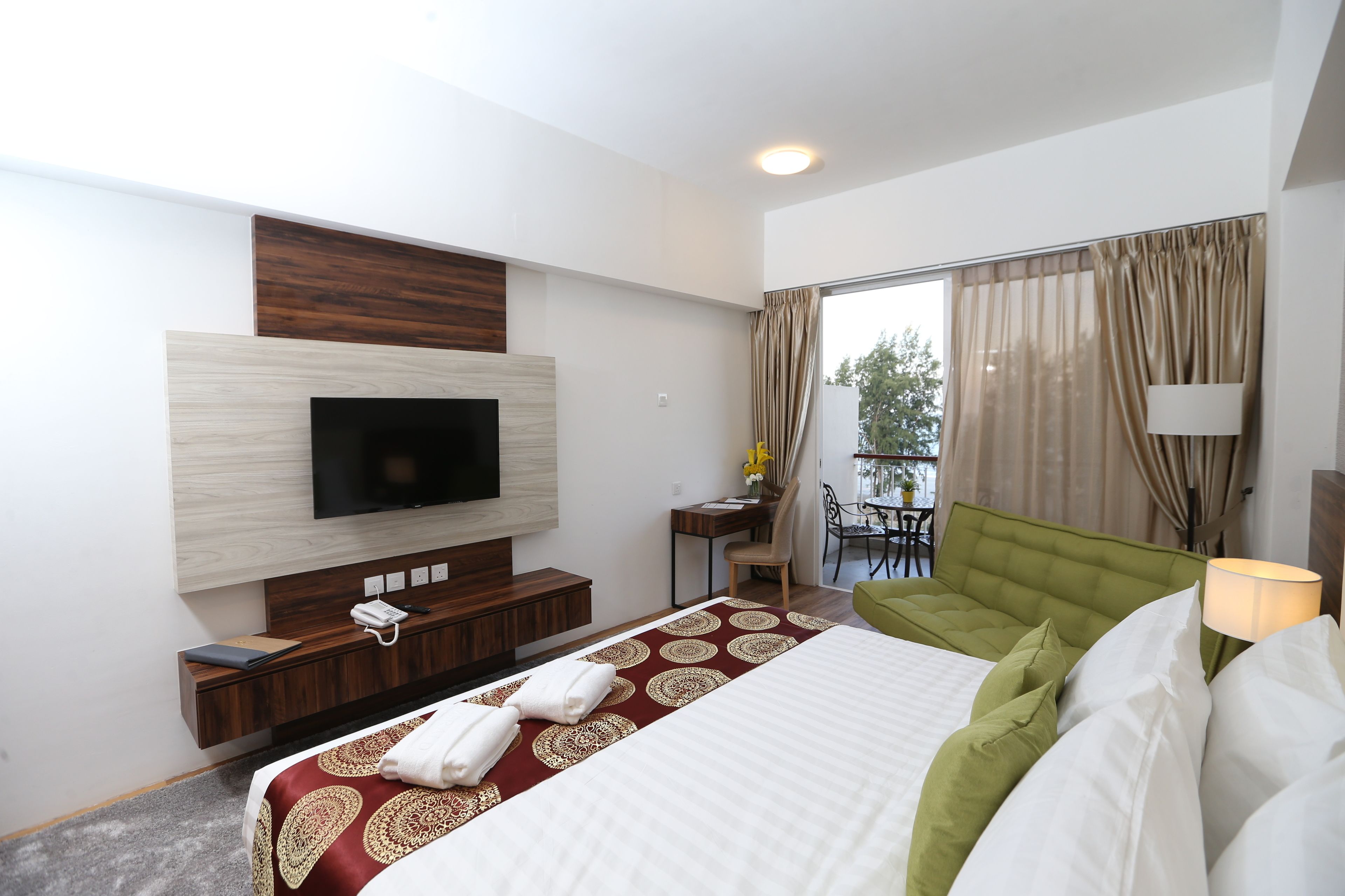 Une chambre d’hôtel dotée d’un grand lit, d’un téléviseur à écran plat fixé au mur, d’un bureau avec une chaise et d’un balcon avec des rideaux.