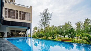 A swimming pool with a modern building in the background, surrounded by greenery. - Amerald Resort Hotel Desaru (Bandar Penawar)