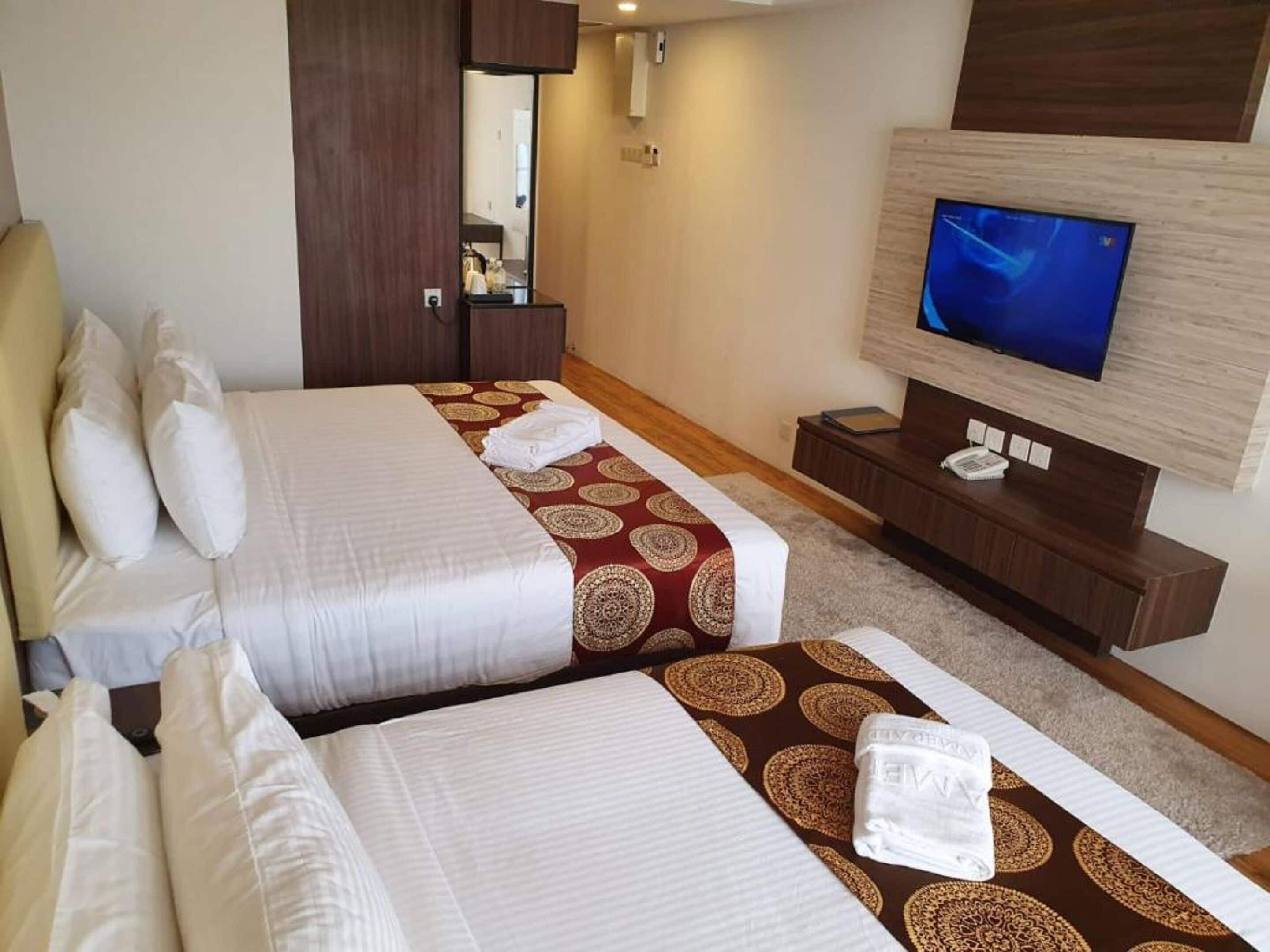 Quarto de hotel com duas camas, televisão, escrivaninha e espelho.
