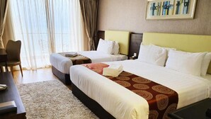 A hotel room with two beds, a desk, a chair, and a large window with curtains. - Amerald Resort Hotel Desaru (Bandar Penawar)