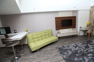 Una sala de estar moderna con un sofá, un escritorio, un televisor montado en la pared y una silla.